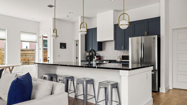 A modern kitchen with dark cabinets, stainless steel appliances, and a central island with stools. - Gorgeous New Build ~Luxury Finishes~ Huge Balcony (Austin)