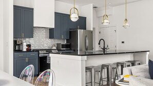 A modern kitchen with dark cabinets, stainless steel appliances, and a central island with bar stools. - Gorgeous New Build ~Luxury Finishes~ Huge Balcony (Austin)