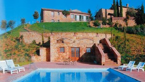 A stone building with a swimming pool, outdoor seating, and a staircase leading to a higher level.