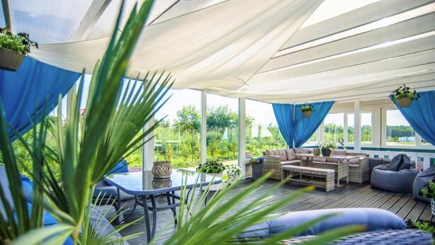 A covered outdoor seating area with wicker furniture, blue curtains, and potted plants. - Rewal Cottage Near the Baltic Beach (Rewal)