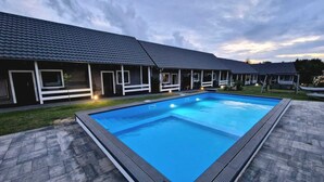 A swimming pool with a tiled deck, surrounded by a building with a dark roof and white trim. - Rewal Cottage Near the Baltic Beach (Rewal)