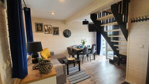 A modern living room with a sofa, coffee table, and dining area. A staircase with a black railing leads to an upper level. - Rewal Cottage Near the Baltic Beach (Rewal)