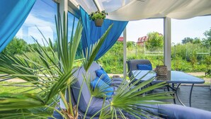 A covered outdoor seating area with a wicker sofa, a table, and a hanging plant. - Rewal Cottage Near the Baltic Beach (Rewal)