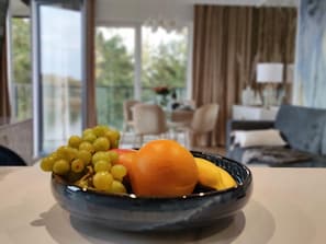 Un saladier de fruits est posé sur une table dans une pièce donnant sur un balcon et une salle à manger.