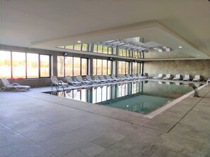 Une piscine intérieure dotée de chaises longues et de grandes fenêtres.