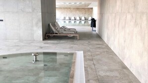 Une piscine intérieure moderne, dotée d’une eau claire, entourée de murs carrelés et agrémentée de quelques chaises longues.