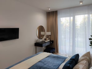 Une chambre d’hôtel moderne, équipée d’un lit, d’un bureau avec une lampe, d’une télévision et d’une grande fenêtre avec des rideaux.