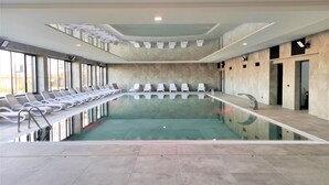 Une piscine intérieure moderne, dotée d’un long bord rectiligne et d’une rangée de chaises longues blanches disposées le long d’un des côtés.