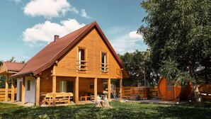 A wooden cabin with a sloped roof, a porch with seating, and a large tree in the background. - Holiday Home Nadole Near Baltic Sea (Gniewino)