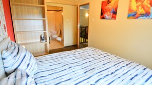 A bedroom with a bed, a wardrobe, and a bathroom visible through an open door. - Cozy Cottage for 2 People Near the Sandy Beach (gmina Bedzino)