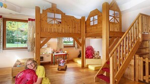 Une pièce spacieuse avec un lit en mezzanine en bois, un espace de jeux et une cuisine à l’arrière-plan.