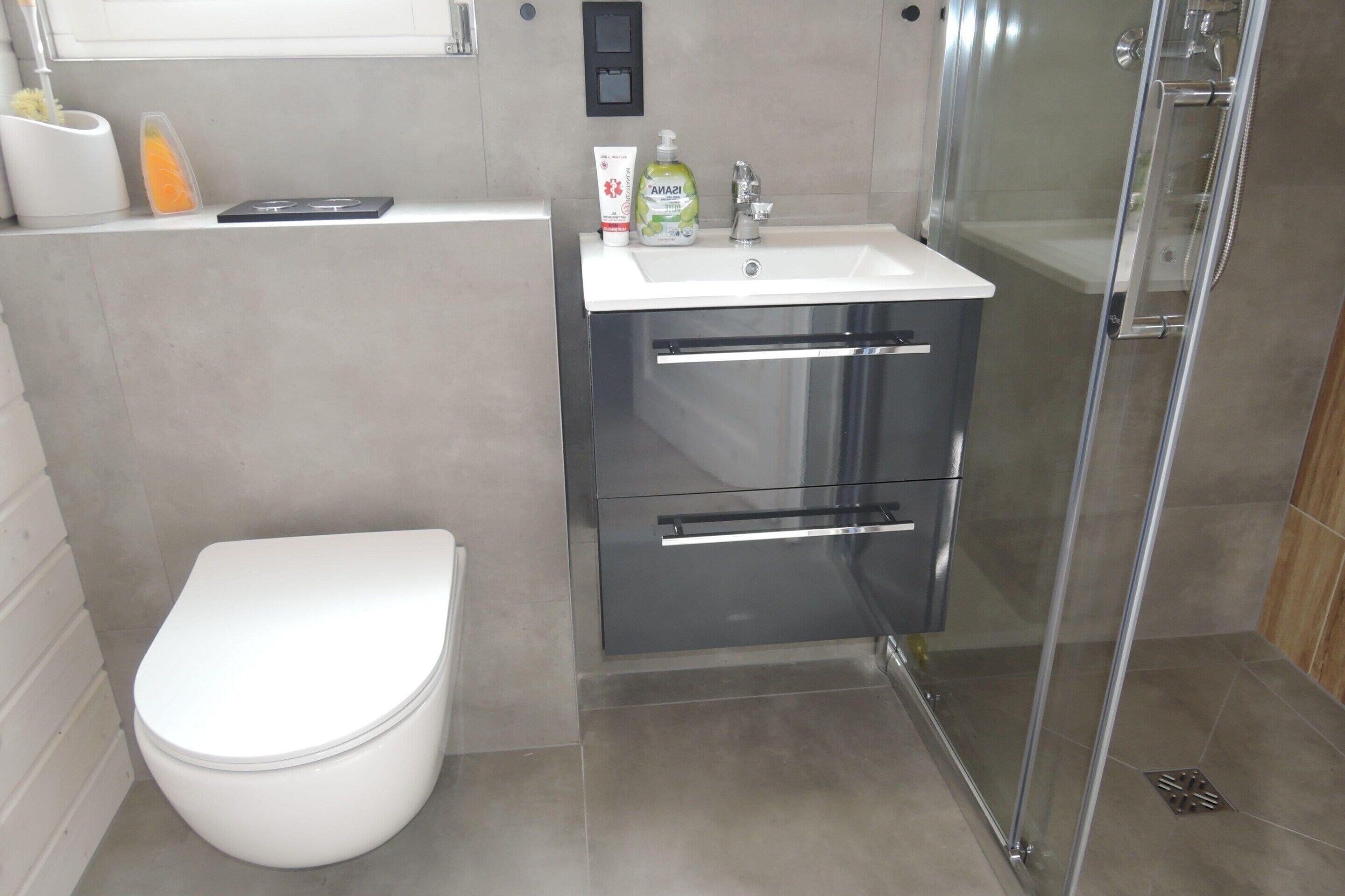 Ein modernes Badezimmer mit Toilette, Waschbecken mit Spiegel und einer Duschkabine aus Glas.