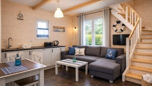 A cozy cabin-style room with a wooden interior, a sofa, a dining table, a kitchen area, and a staircase. - Holiday Home in Rewal Near Baltic Beach (Rewal)