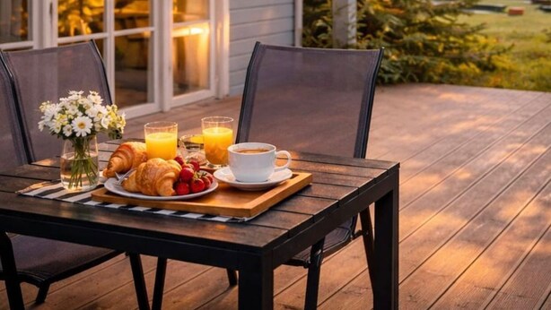 A wooden deck with a table set for breakfast, including croissants, fruit, and coffee. - Holiday Home in Rewal Near Baltic Beach (Rewal)