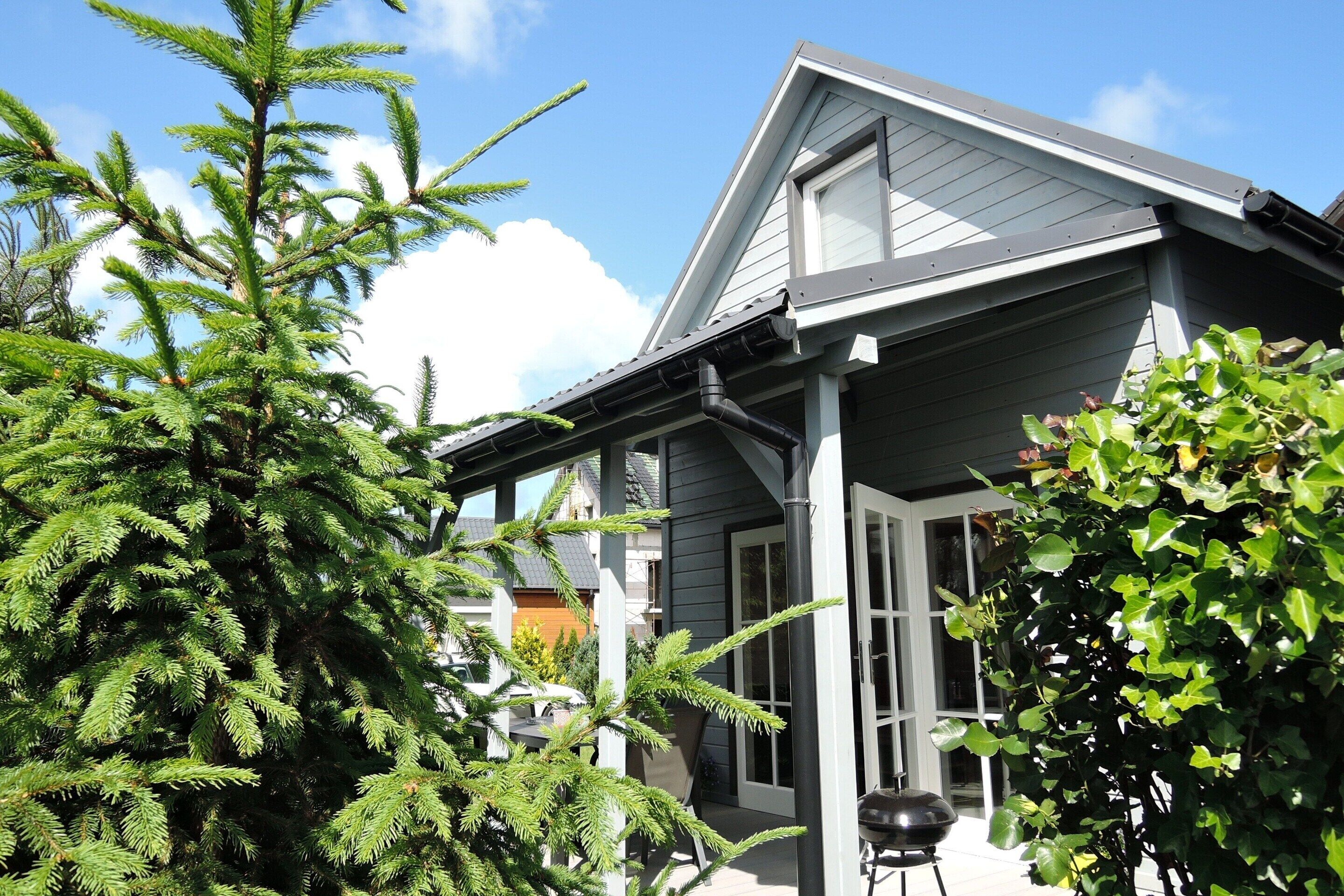 Een huis met een grijs dak, witte details en een veranda met een bloempot.