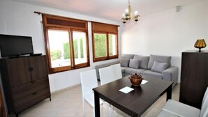 A modern living room with a sofa, dining table, and TV. - Apartments La Pineda, Playa de Pals (Pals)