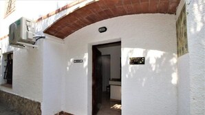 A white building with a brick archway entrance, a sign indicating a business, and a small outdoor area with a plant. - Apartments La Pineda, Playa de Pals (Pals)