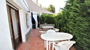 An outdoor patio with white tables and chairs, a round table, and a large green hedge. - Apartments La Pineda, Playa de Pals (Pals)