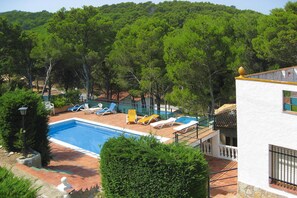 A swimming pool with lounge chairs, surrounded by trees and a white building with a tiled roof. - Apartments La Pineda, Playa de Pals (Pals)