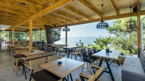 An outdoor dining area with wooden tables and chairs, a view of the sea, and hanging light fixtures. - Gerakini Holiday Home With a Balcony (Polygyros)