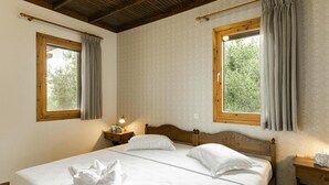 A bedroom with a wooden bed, two windows with curtains, a bedside table with a lamp, and a wall-mounted clock. - Gerakini Holiday Home With a Balcony (Polygyros)