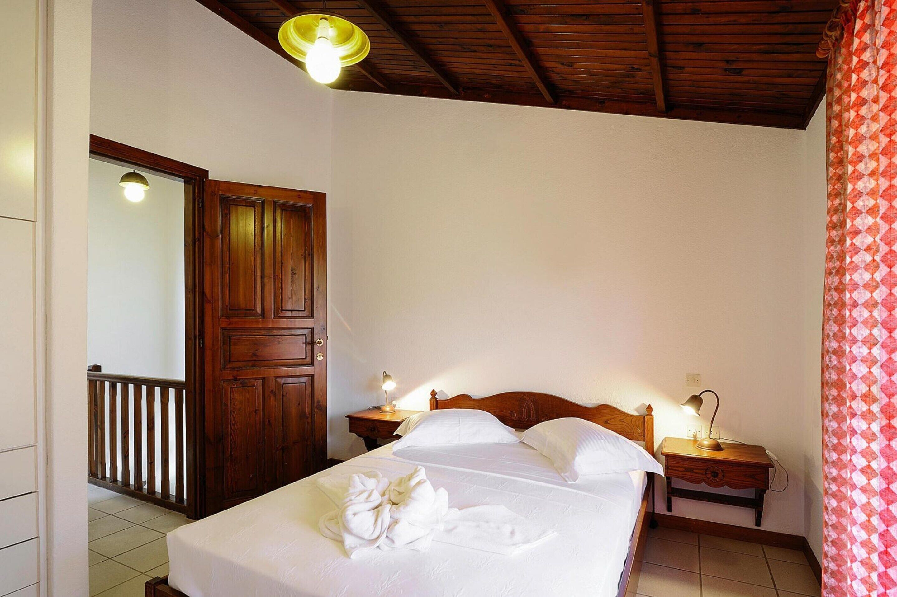 Un dormitorio con una cama de madera, dos mesitas de noche con lámparas, una puerta de madera y una cortina estampada.