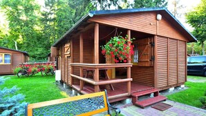Une cabane en bois avec une véranda, un banc et des plantes en suspension.