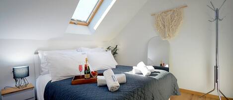 A modern bedroom with a skylight, a bed with a dark quilt, a bedside table with a lamp, and a floor lamp.