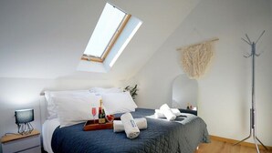 A bedroom with a skylight, a bed with a dark quilt, a bedside table with a lamp, a mirror, and a floor lamp. - Holiday Home in Mielenko Near Seaside Beach (Mielno)