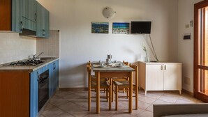 A kitchen with blue cabinets, a dining table with chairs, a stove, and a TV mounted on the wall. - Holiday Resort, Budoni (Budoni)