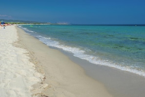 Ein Strand mit klarem türkisblauem Wasser, sandigem Ufer und sanften Hügeln im Hintergrund.