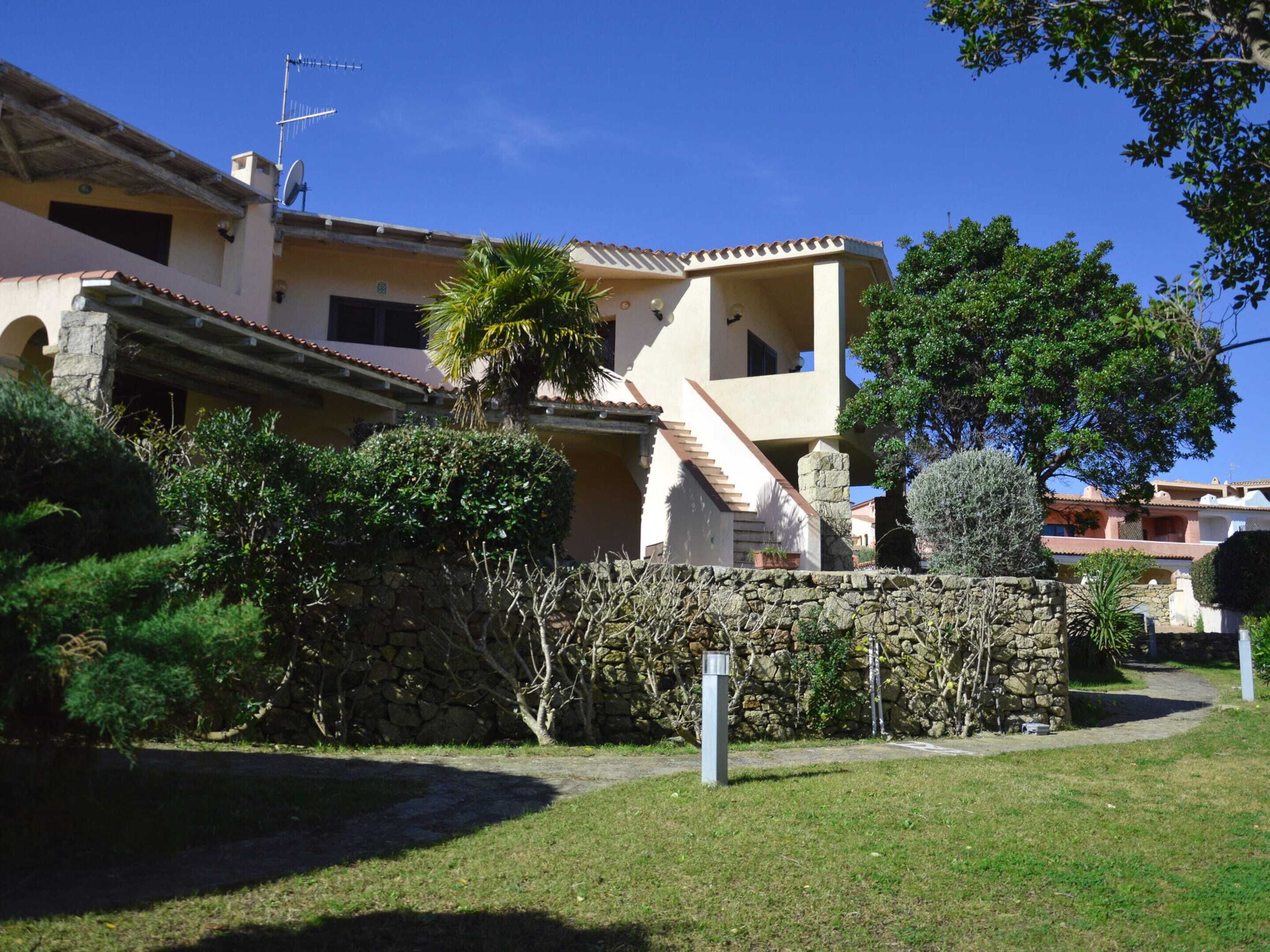 A Mediterranean-style villa with a stone wall, a palm tree, and a clear blue sky.