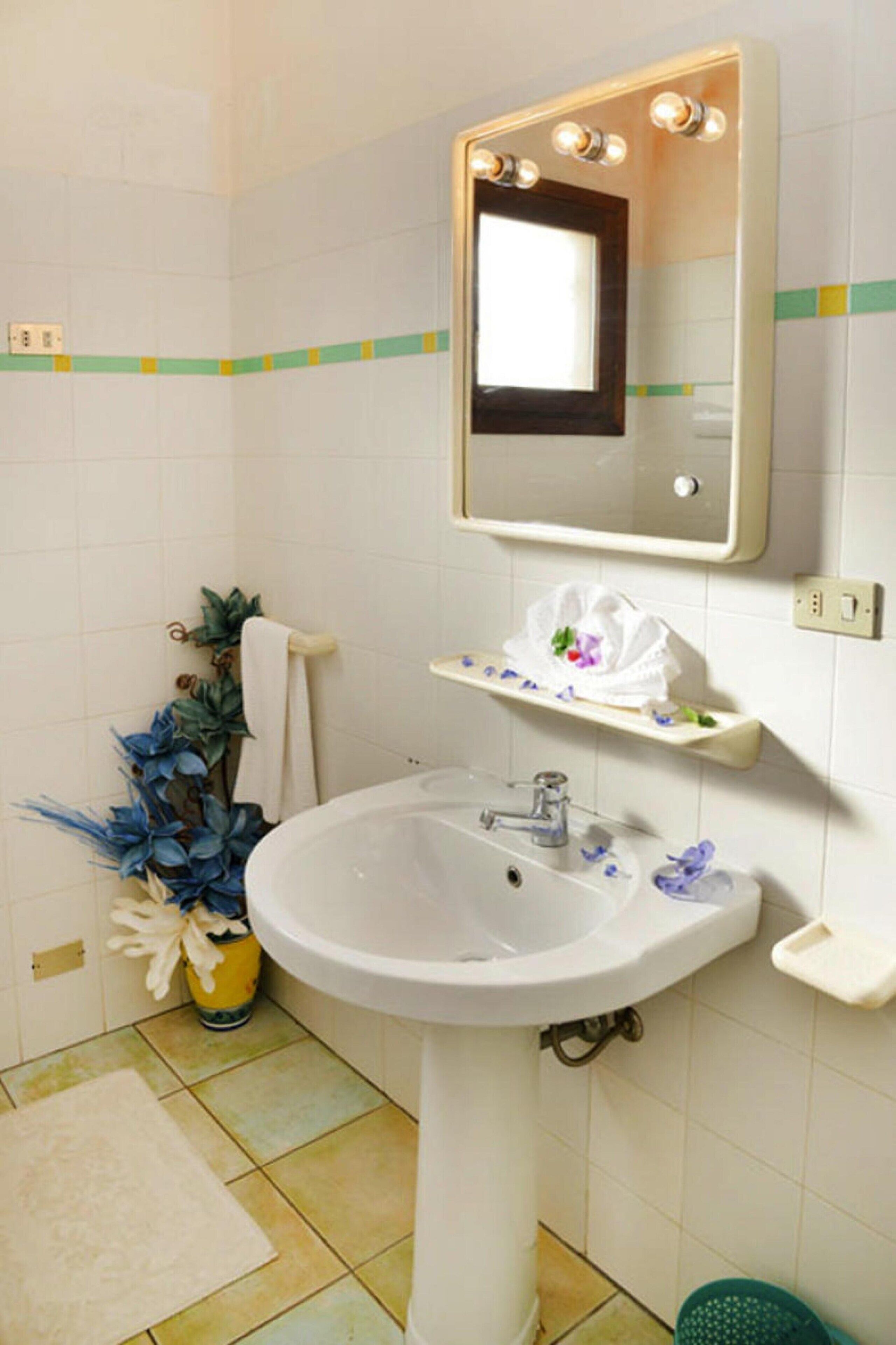 Un bagno con lavandino bianco, specchio e portasciugamani.