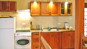 Een keuken met houten kastjes, een witte koelkast, een oven, een spoelbak en een fornuis.