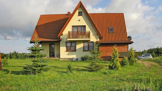 Een huis met twee verdiepingen, voorzien van een rood pannendak, een balkon en een kleine tuin.
