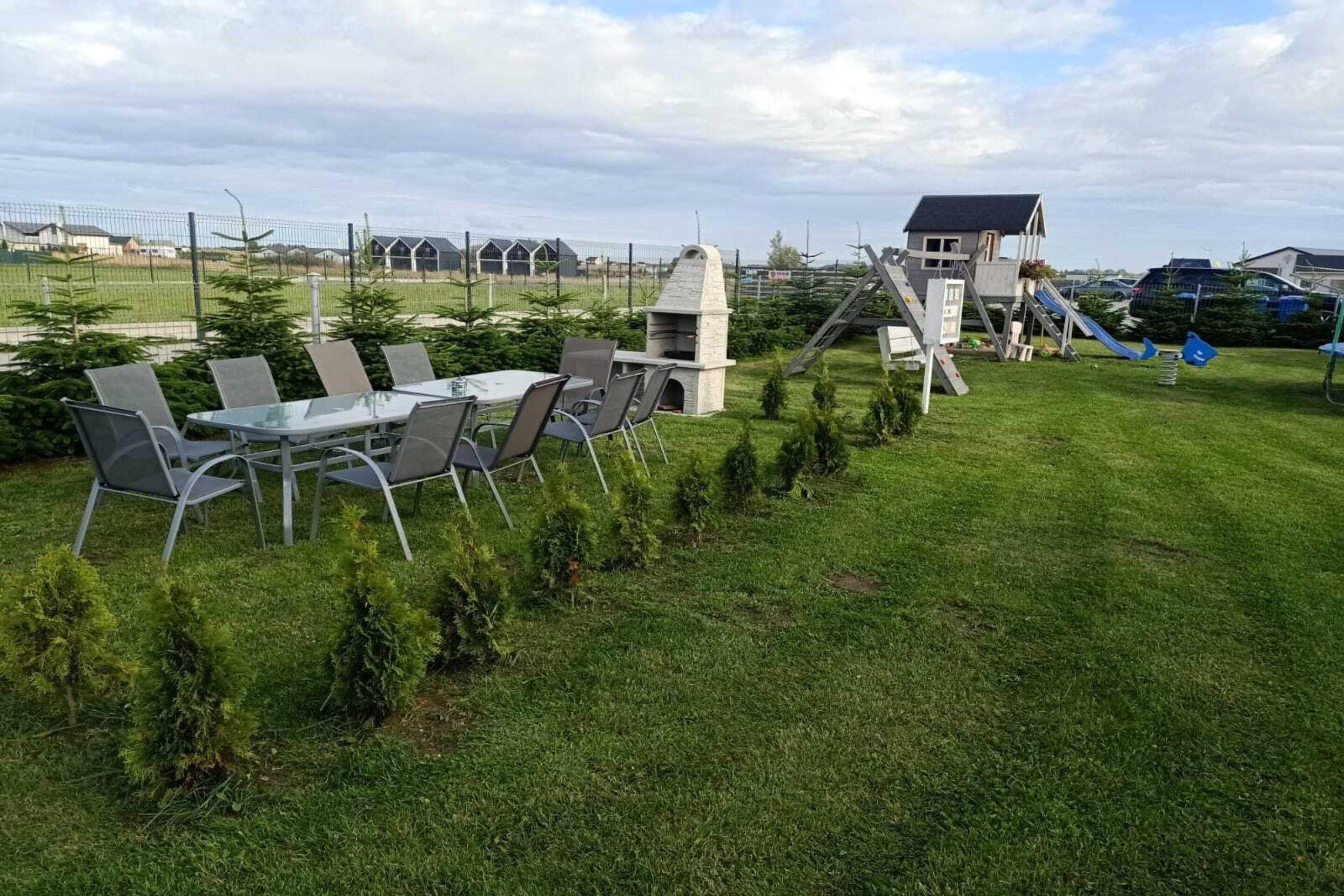 Ein grünes Freigelände mit Tisch und Stühlen, einer Spielanlage und einem Gebäude im Hintergrund.