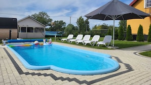 A rectangular swimming pool with a zigzag edge, surrounded by white lounge chairs and a large umbrella.