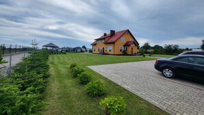 A yellow house with a red roof, a paved driveway, and a car parked on the right.
