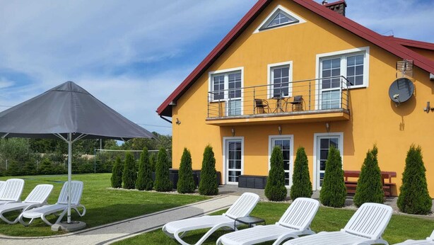 A yellow building with a red roof, white windows, and a balcony with outdoor furniture.