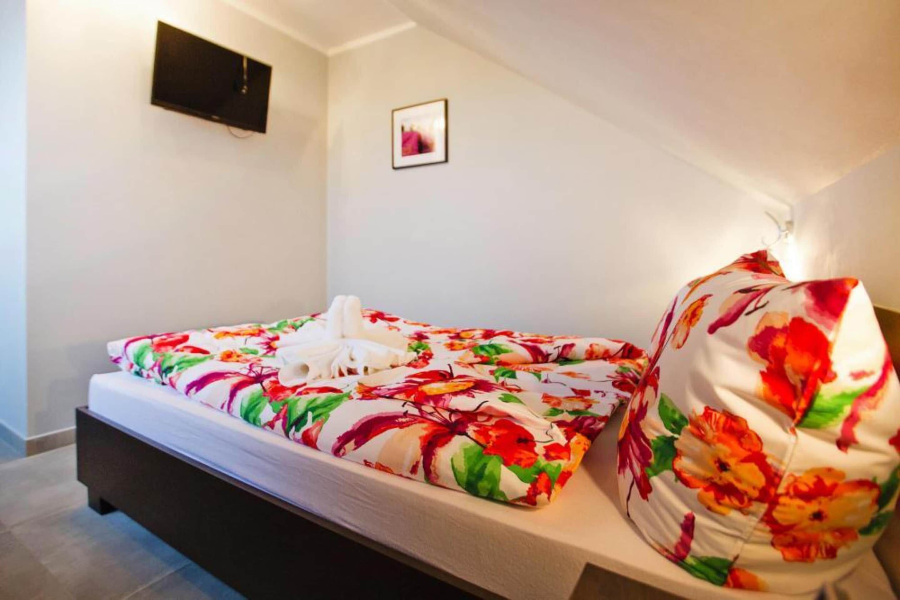 Een slaapkamer met een bed, een kussen, een wandtelevisie en een lijst met een afbeelding.