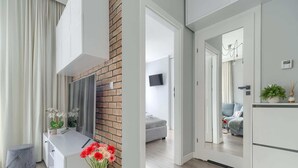 Ett modernt vardagsrum med en vit soffa, ett soffbord och en vas med blommor. En vägg är klädd med tegelstenar och en platt-TV är monterad på väggen.