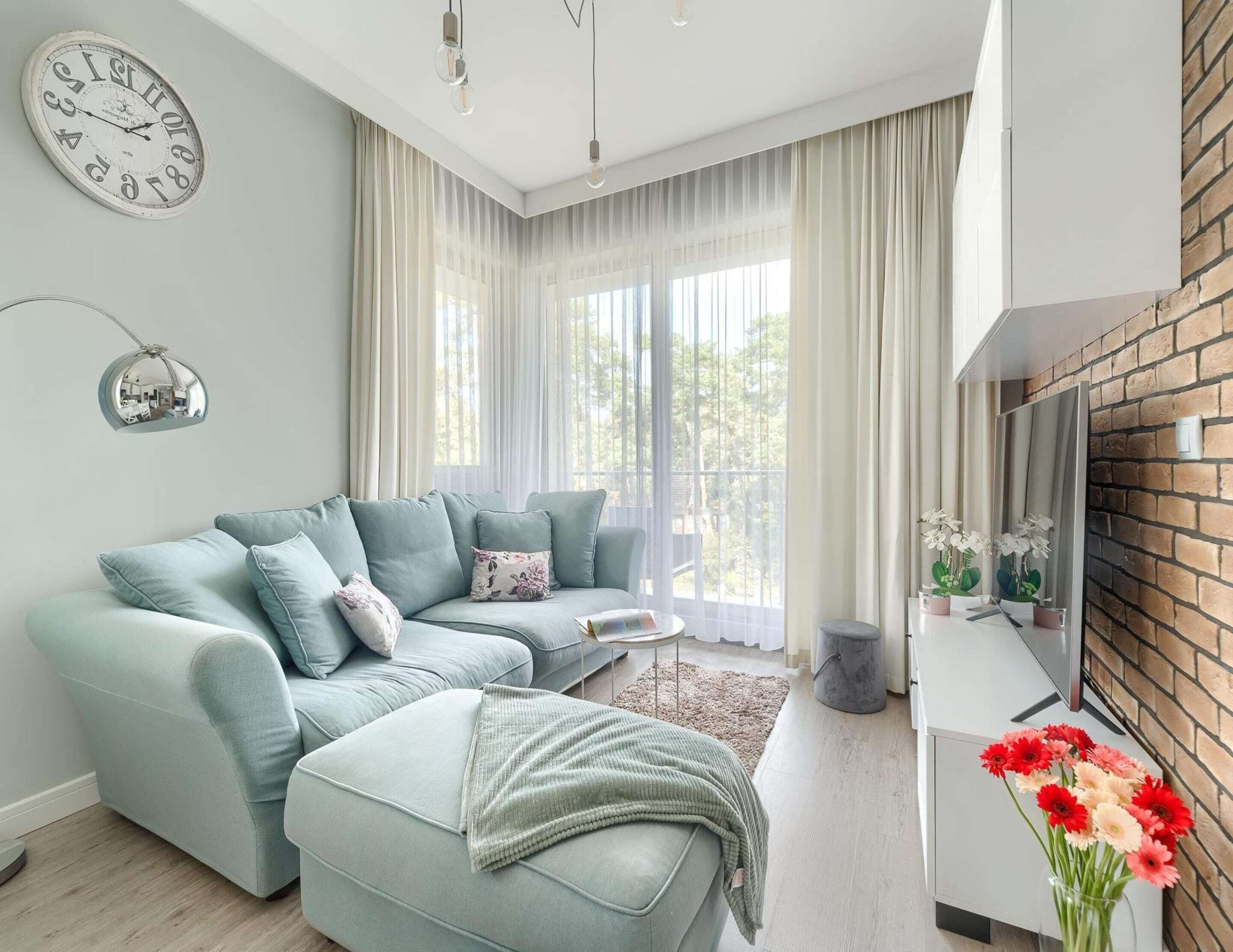 A modern living room with a sectional sofa, a round coffee table, and a large window with sheer curtains.