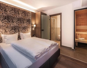 A modern hotel room with a large bed, a wooden headboard, a shower area, and a sauna. - Apartment in Ischgl With Sauna (Ischgl)