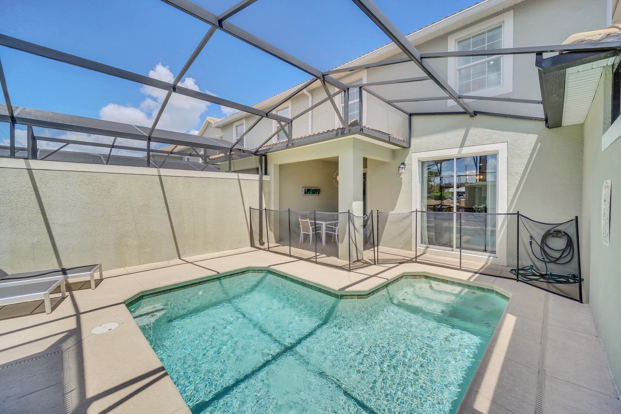 A swimming pool with a glass enclosure, a covered patio area, and a view of a residential building.