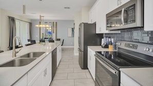 A modern kitchen with stainless steel appliances, a double sink, and a central island. - EV_4958 - 4BR / 3BA Storey Lake Townhome near to Disney, Private Pool & Resort (Kissimmee)