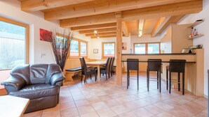 A spacious living area with a wooden ceiling, a dining table, and a bar area with stools. - Chalet in Krimml Near Europe's Highest Waterfall (Krimml)