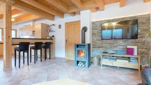A cozy living room with a fireplace, a TV mounted on a stone wall, and a dining area with chairs. - Chalet in Krimml Near Europe's Highest Waterfall (Krimml)