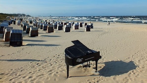 Une plage bordée de rangées de chaises de plage rayées, avec un grand piano en premier plan.