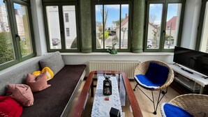Un salon avec un canapé, une table, un téléviseur et de grandes fenêtres aux cadres verts.