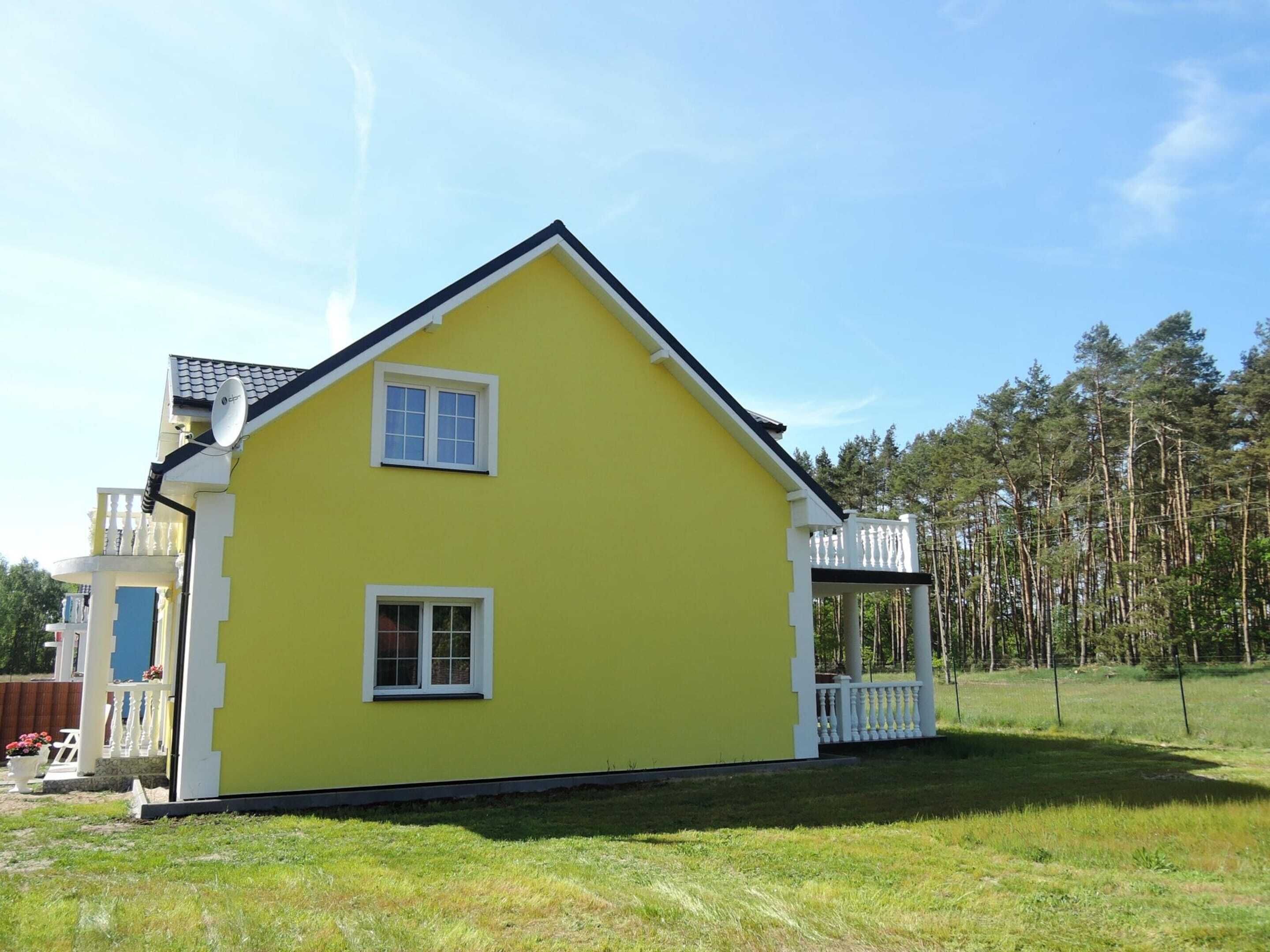 A two-story yellow house with a balcony, surrounded by a grassy yard and trees.
